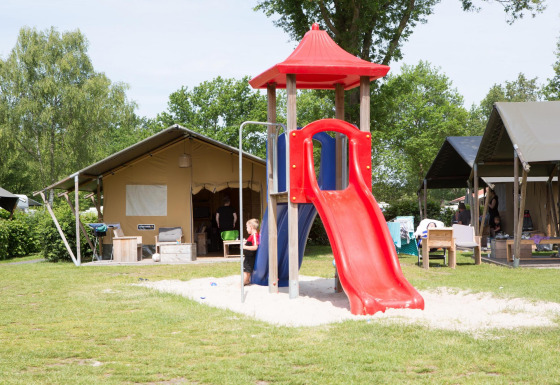 Bambini giocano su uno scivolo rosso davanti a tende safari al Camping 't Veld nei Paesi Bassi.