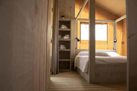 Comfort Safari tent bedroom with a double bed and shelving, at Camping ‘t Veld in the Netherlands.