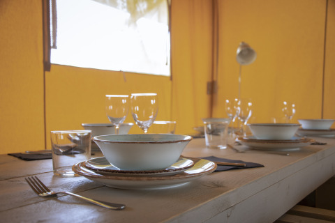 Mesa preparada con platos y vasos en el interior de una tienda Comfort Safari en Camping 't Veld, Países Bajos.