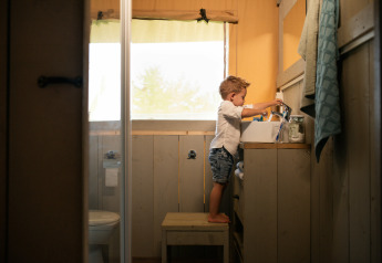 Een kind staat op een krukje en wast zijn handen bij de wasbak in de Comfort Safari tent in Nederland.