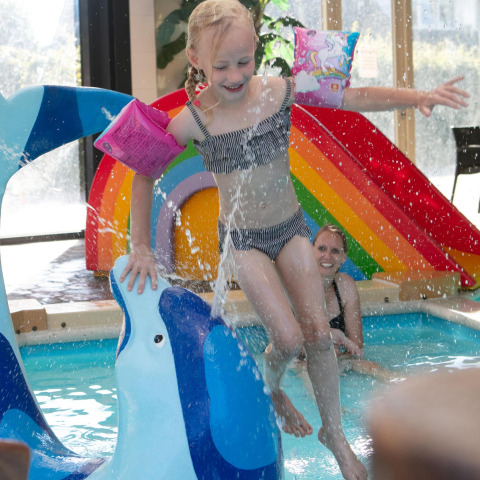 Bambina gioca in piscina con scivolo arcobaleno e delfino al Comfort Safari tent, Camping 't Veld.
