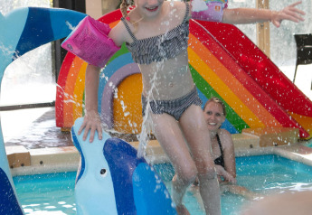 Mädchen spielt im Innenpool mit bunter Regenbogenrutsche und Delphinfigur im Comfort Safari-Zelt, Camping 't Veld.