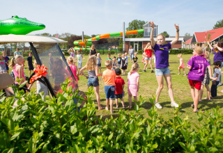 Kinder und Erwachsene spielen auf einer Campingwiese mit Safarizelten und Wasserrutschen im Hintergrund.