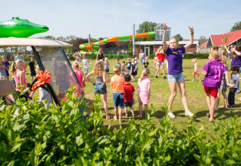 Des enfants et des adultes jouent ensemble sur un terrain de camping avec tentes safari et toboggans derrière.