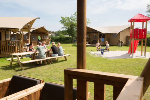 Familier nyder udendørs ophold foran safaritelte med legeplads på Camping 't Veld i Holland.