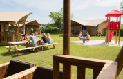 Familier nyder udendørs ophold foran safaritelte med legeplads på Camping 't Veld i Holland.