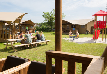 Famiglie si rilassano davanti a tende safari con parco giochi al Camping 't Veld nei Paesi Bassi.