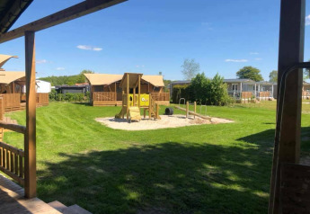 Tienda safari de lujo en Camping 't Veld en Países Bajos con zona de juegos y cabañas bajo un cielo azul.