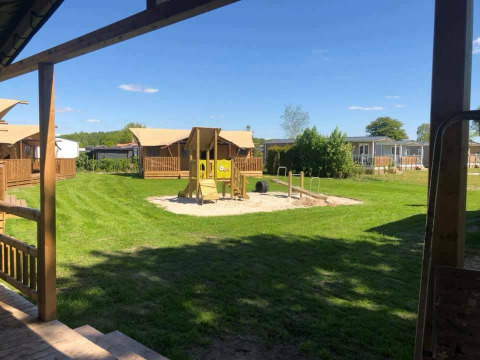 Safari tent de luxe at Camping 't Veld in the Netherlands, featuring a playground and lodges under blue sky.