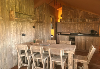 Interior de Safari tent de luxe en Camping 't Veld, Países Bajos, con mesa de madera y cocina rústica.