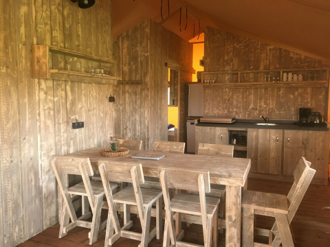 Interieur van de luxe safaritent op Camping 't Veld in Nederland, met houten tafel en keukentje.
