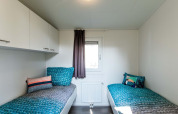 Modern lodge room with two single beds, colorful pillows, overhead cabinets, and a central window.