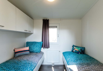 Habitación moderna de la cabaña con dos camas individuales, cojines coloridos y una ventana central.