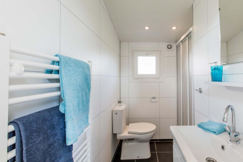Moderne badkamer met witte tegels, douche, toilet en blauwe handdoeken bij Rialto Wellness Spa, Beekbergen.