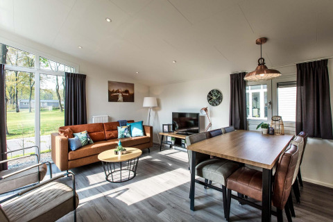 Sala de estar moderna y luminosa con ventanales, sofá marrón y comedor en Rialto Wellness, Beekbergen, Países Bajos.