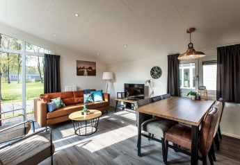 Sala de estar moderna y luminosa con ventanales, sofá marrón y comedor en Rialto Wellness, Beekbergen, Países Bajos.