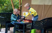 Tre børn leger et brætspil udenfor i en safaritelt på Camping 't Veld, Holland, omgivet af natur.