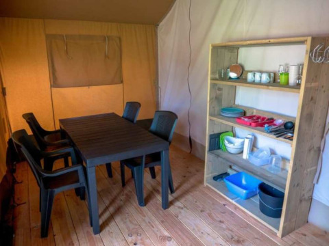 Interior de una tienda safari en Camping 't Veld, Países Bajos, con mesa, sillas y estantería de cocina.