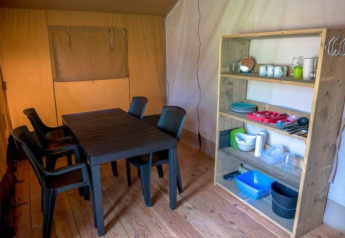 Interior de una tienda safari en Camping 't Veld, Países Bajos, con mesa, sillas y estantería de cocina.
