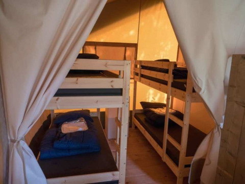 Interior de una tienda safari con literas en Camping 't Veld en los Países Bajos, iluminada por la luz del día.