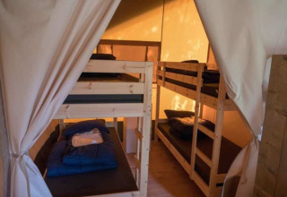 Binnenkant van een safaritent met stapelbedden op Camping 't Veld in Nederland, verlicht door zonlicht.