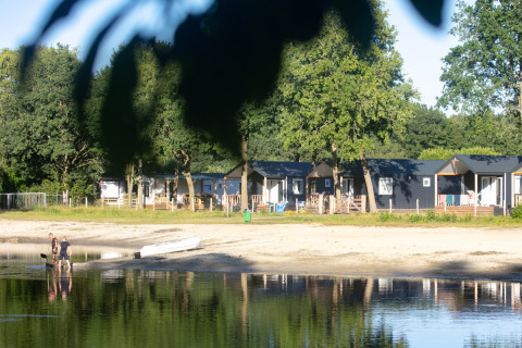 Casas de playa en Camping 't Veld, Países Bajos, junto al lago con personas y una canoa en la orilla.