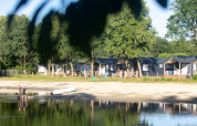 Cabanes de plage au Camping 't Veld aux Pays-Bas, au bord du lac avec des personnes et un canoë.