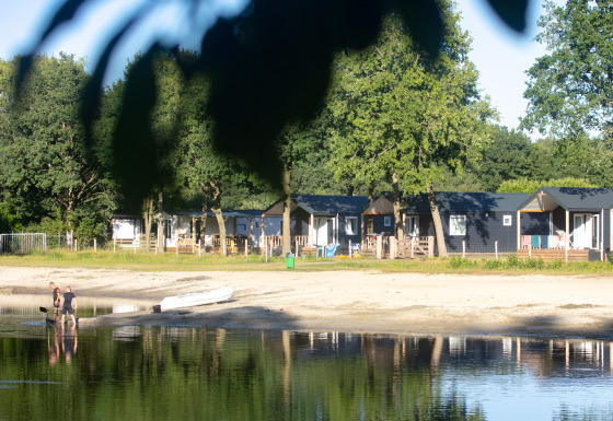 Strandhäuser im Camping 't Veld in den Niederlanden am Seeufer mit Menschen am Wasser und Boot.