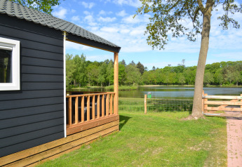 View from the beach house lodge at Camping 't Veld, Netherlands, showing pond, trees and green lawn.