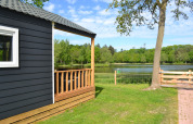 View from the beach house lodge at Camping 't Veld, Netherlands, showing pond, trees and green lawn.