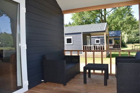 Porche de madera con muebles negros, vista a casas de playa en Camping 't Veld, Países Bajos.