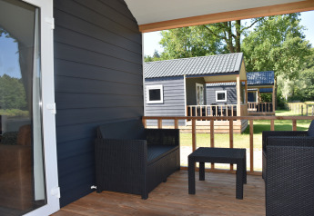 Porche de madera con muebles negros, vista a casas de playa en Camping 't Veld, Países Bajos.