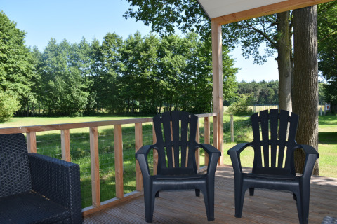 Due sedie nere su veranda in legno con vista sui prati e alberi a Beach house, Camping 't Veld, Paesi Bassi.