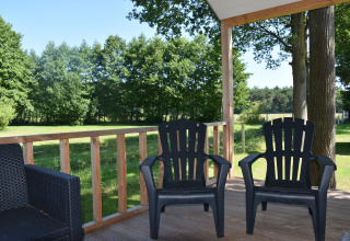 Two black outdoor chairs on a wooden porch overlooking green fields and trees at Beach house, Camping 't Veld.