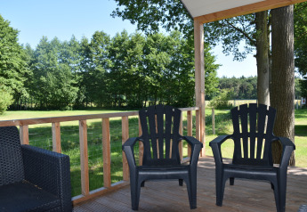 Two black outdoor chairs on a wooden porch overlooking green fields and trees at Beach house, Camping 't Veld.