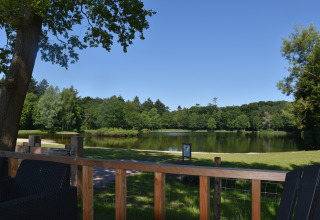 Udsigt fra Beach house-lodgen ved Camping 't Veld i Holland med sø, grønne træer og blå himmel.