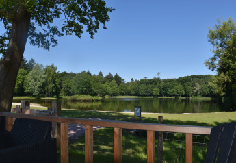 Vista dalla lodge Beach house al Camping 't Veld nei Paesi Bassi, con lago, alberi e cielo sereno.