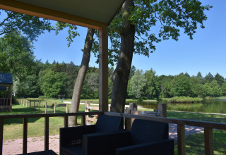Vista desde la Beach House lodge en Camping 't Veld, Países Bajos, con terraza, lago y vegetación.