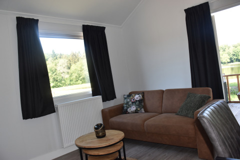 Woonkamer van Beach House lodge op Camping 't Veld in Nederland, met bank en uitzicht op de natuur.