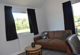 Woonkamer in Beach House-lodge bij Camping 't Veld, Nederland, met zetel en zicht op buiten.