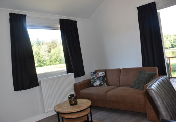 Living room in Beach House lodge at Camping 't Veld, Netherlands, with a sofa and scenic outdoor view.