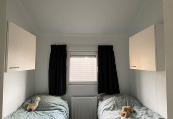 Zwei Einzelbetten mit Spielzeug in einem kompakten, hellen Zimmer in einer Lodge am Campingplatz 't Veld.