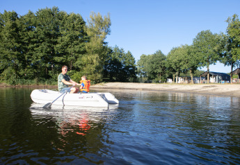 Un homme et un enfant en bateau gonflable sur le lac près de Beach house à Camping 't Veld, Pays-Bas, entourés d’arbres.