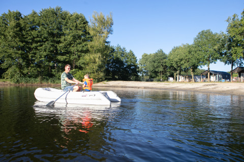 A man and child in an inflatable boat on a lake at Beach house, Camping 't Veld, Netherlands, with trees around.