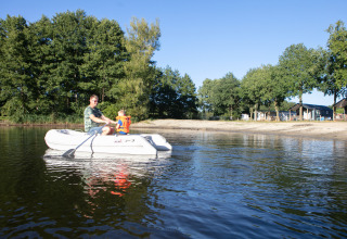 Un hombre y un niño en bote inflable en el lago junto a Beach house en Camping 't Veld, Países Bajos, rodeados de árboles.