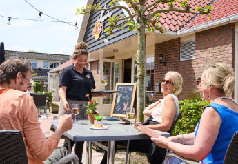 Terraza al aire libre en Beach house, Camping 't Veld, Países Bajos, personas disfrutan comida y bebida.