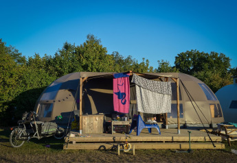 Glamping accommodatie met een koepeltent, fiets vooraan en wasgoed hangend op de veranda.