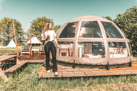 Mujer junto a una tiny house Riverdome con baño y jacuzzi en Holiday Park Mölke, Países Bajos.