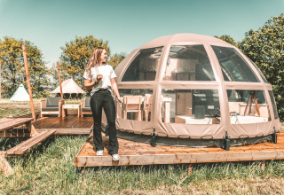 Mujer junto a una tiny house Riverdome con baño y jacuzzi en Holiday Park Mölke, Países Bajos.