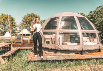 Mujer junto a una tiny house Riverdome con baño y jacuzzi en Holiday Park Mölke, Países Bajos.